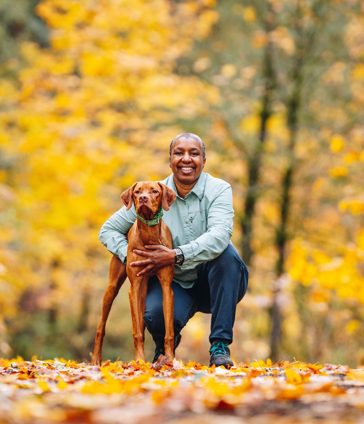 09_kronda_yoda_kneeling_cropped Kronda kneeling and holding her Vizsla puppy Yoda in the woods with fall foliage in the background